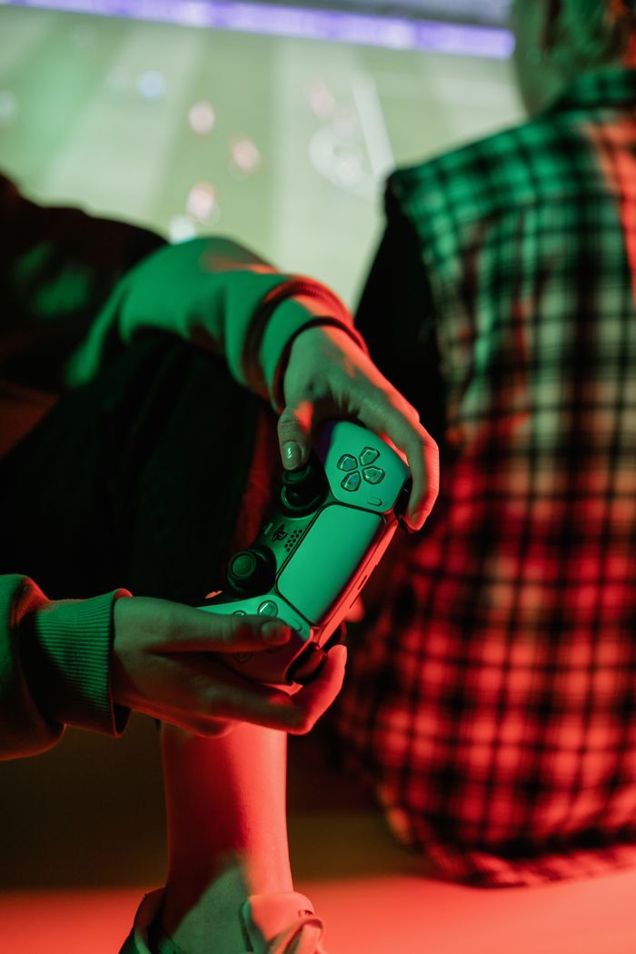 A gamer holds a video game controller in a warmly lit, cozy setting with a friend nearby.